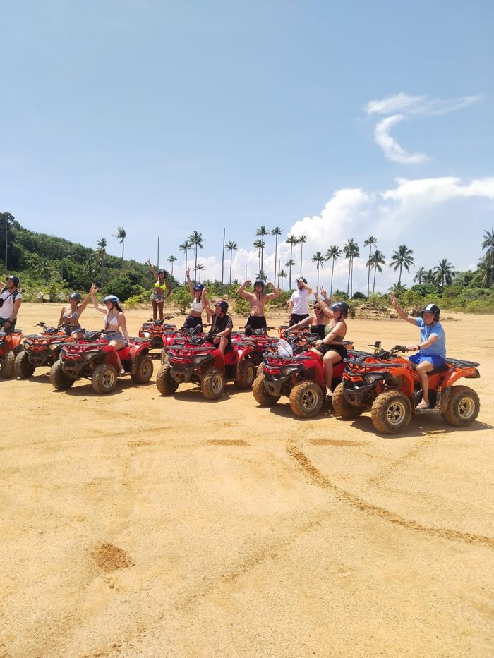 Mixed group on ATV quads under tall palm trees, Koh Phangan