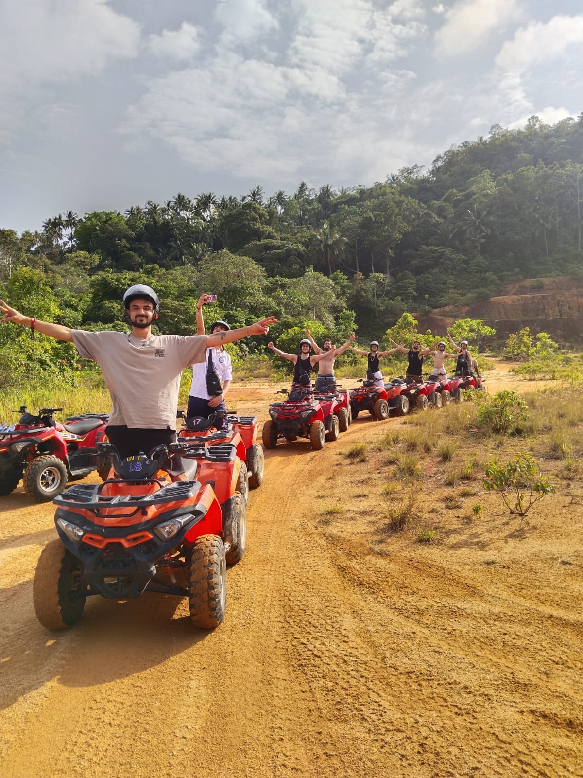 Group riding ATV quads up a red-dirt jungle trail on Koh Phangan, Thailand